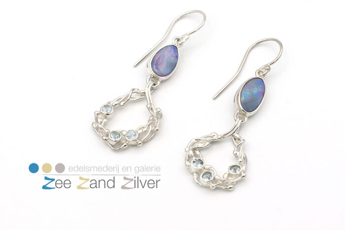 Zilveren (925) oorbellen bestaande uit getwijnde draden waar tussen natuurstenen topaas (licht blauw) gezet zijn. Onder het oor hangt een opaal gezet in zilveren zetkastje.