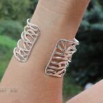 Brede zilveren armband bestaande uit ovale draden die een speels patroon volgen